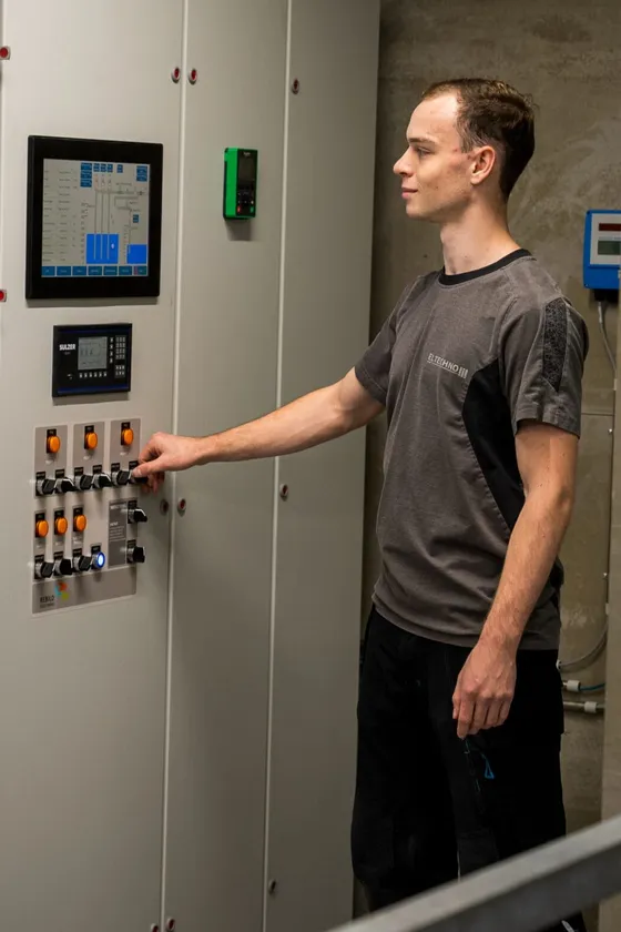 Mand betjener industrielt kontrolpanel i teknikrum